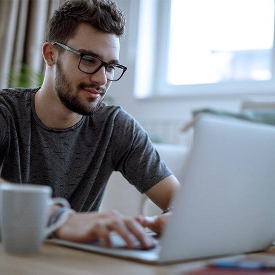 Man sitting at a table with laptop and cup of coffee staying connected with Viasat's satellite internet and the FCC's Affordable Connectivity Program.